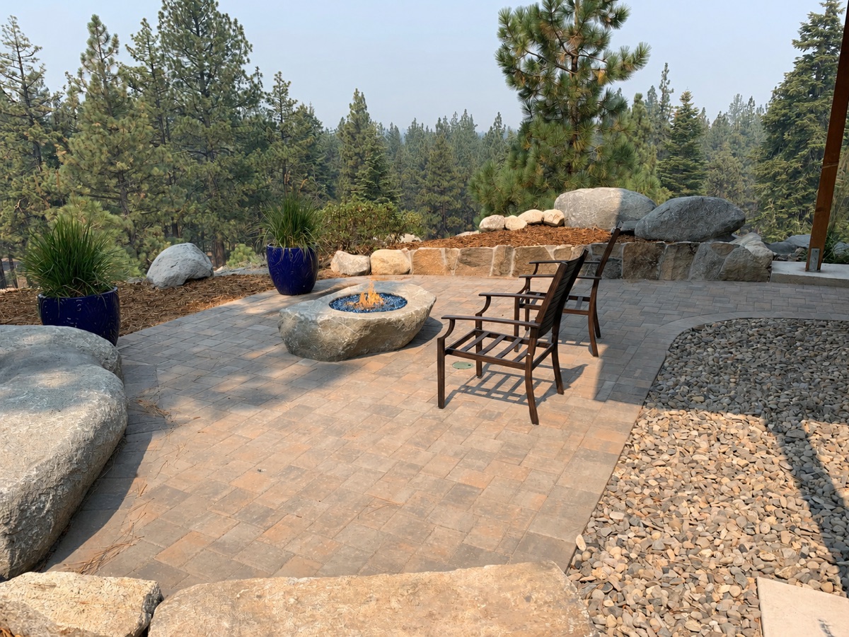 Paver patio with boulder fire feature, seating, retaining wall, granite boulders, and Tahoe pine backdrop
